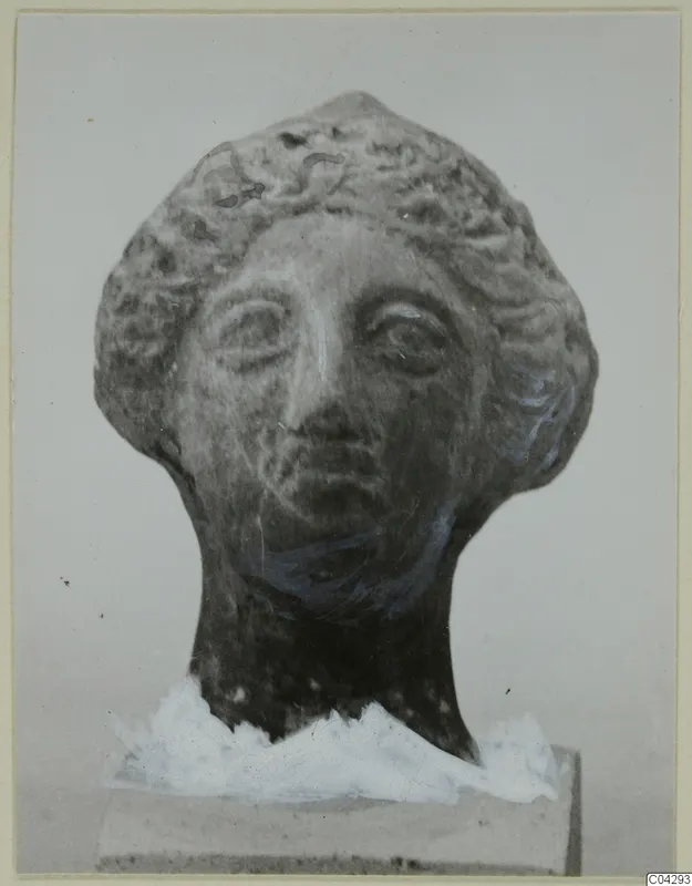 Terracotta head with curled hair, its neck resting on a plain block, photographed against a grey background.