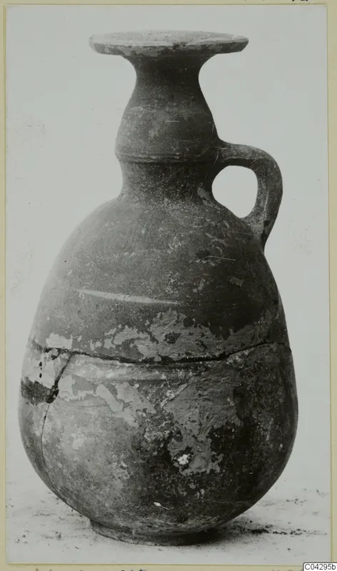 Pottery vessel with a single handle, flaring rim and worn surface, shown against a plain background