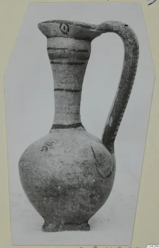 Painted pottery jug with a tall neck, a strap handle and dark horizontal bands, photographed on a light background.