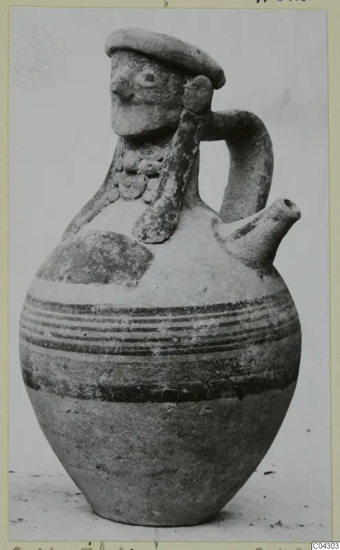 Jug with a modelled human face on the neck, a strap handle, a spout and dark painted bands on the body.