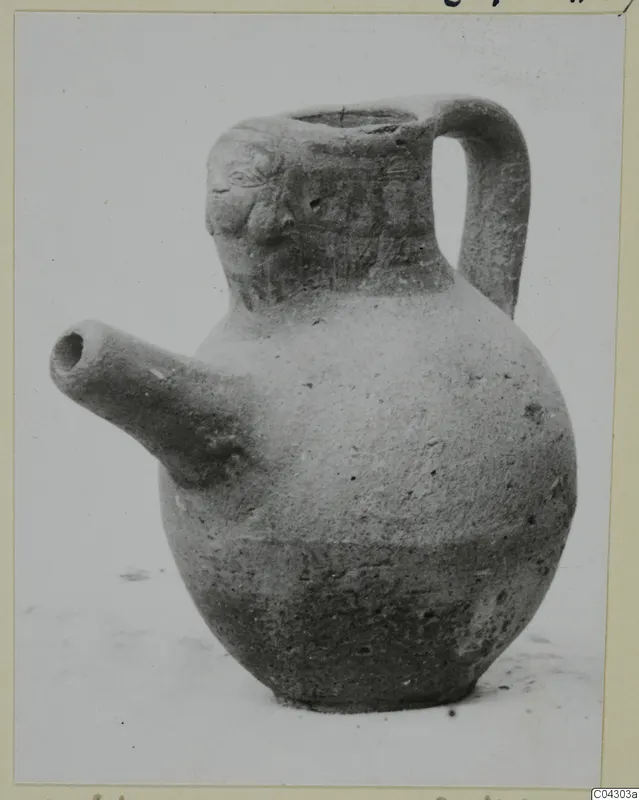 Pottery jug with a side spout, a strap handle and modelled face-like features on the neck