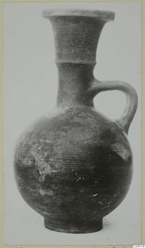 Pottery jug with a flared neck and a single strap handle, shown from the side against a pale background.