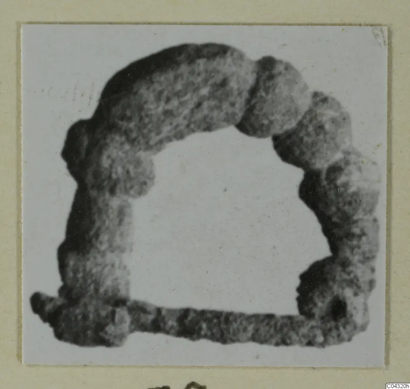Corroded object from Amathus tombs 2-26, shown as an open, arch-shaped frame with a straight bar along the base.