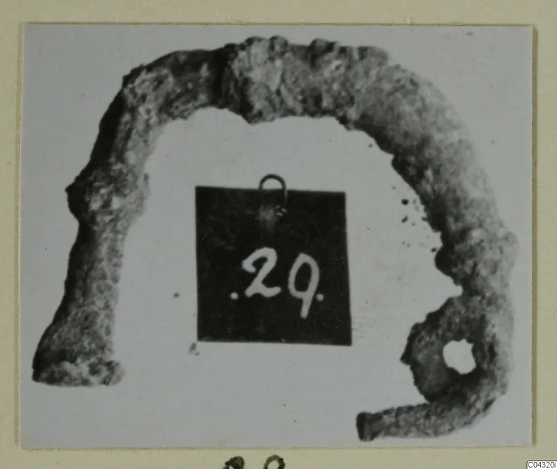 Corroded bronze part with a loop, photographed with a number label, from Amathus