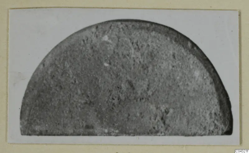 Part of a stone object: a semicircular grey stone fragment with a grainy surface, photographed on a card mount