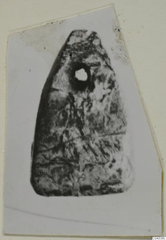 Stone object with a drilled hole near its top, shown as a photograph on a card mount