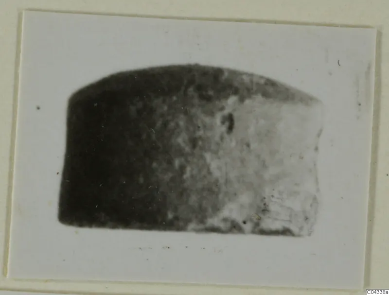 Blurred photograph of a dark stone object with a rounded top, mounted on a cream card