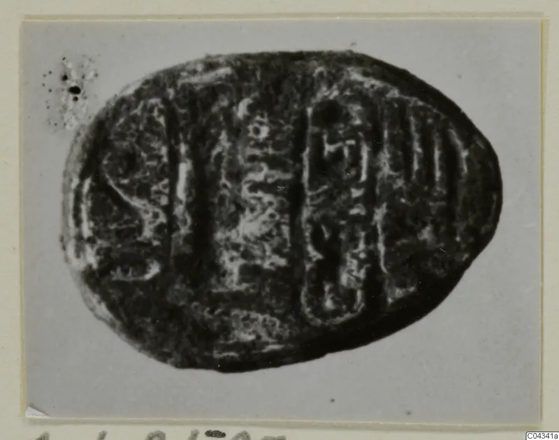 Oval dark stone seal with incised signs on its flat base, photographed on a grey card mount