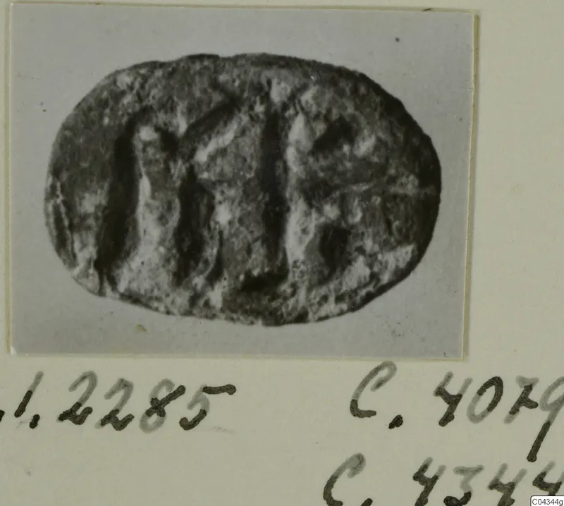 Oval seal or gem with carved upright lines and a worn surface, photographed on a grey backdrop