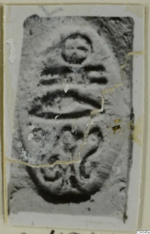 Enlarged photograph of an engraved seal or gem, with a small circle above horizontal bands and a curled motif below.