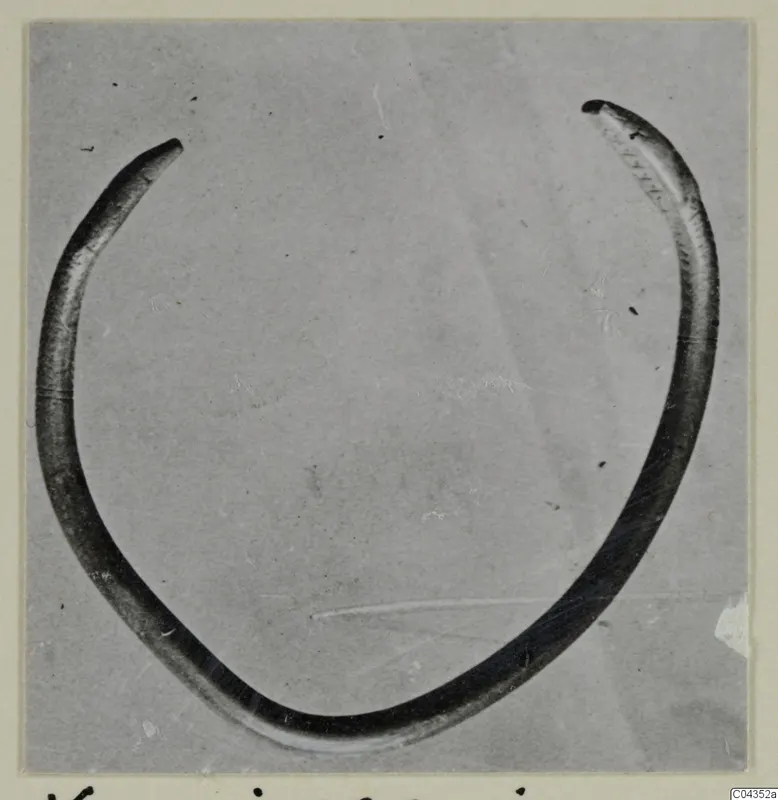 Open ring of silver, thin and tapering to a point at each end, photographed on a grey background