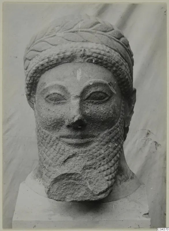 Limestone sculpted head of a bearded man in a band-and-leaf headdress, on a square base.