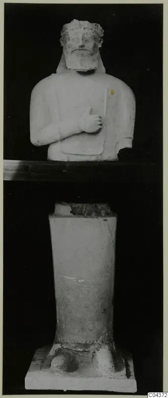 Parts of a stone statue: a bearded bust with its hand raised to the chest, shown above a separate tapering pedestal