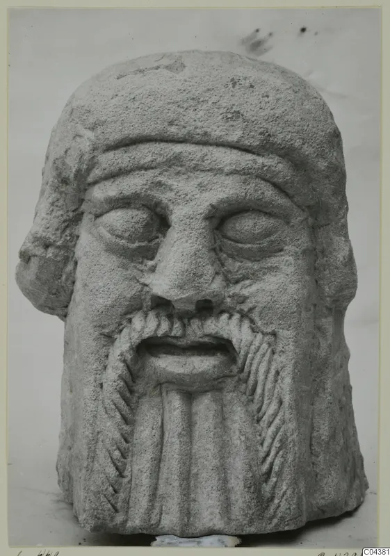 Limestone head of a bearded male figure from Soli, face and beard carved in relief.
