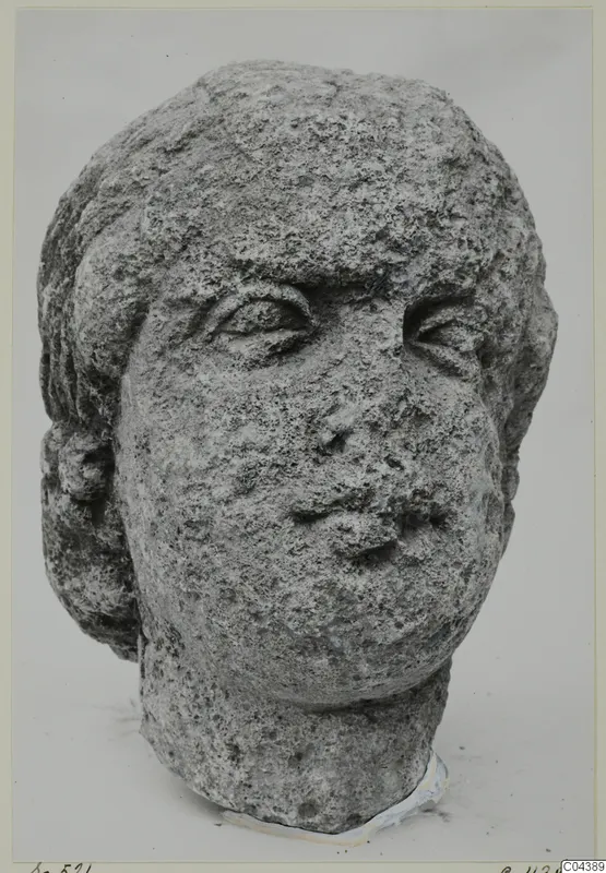 Stone head from Soli, a carved male or female face with hair framing it, shown against a pale background.
