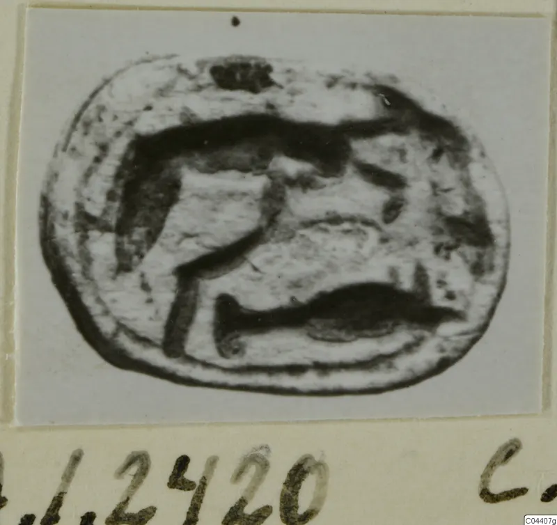 Oval engraved seal stone with a dark incised design, shown on a card mount