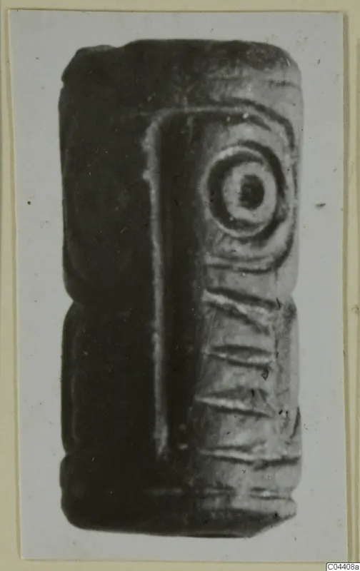 Dark stone seal, rectangular and elongated, with a concentric circle motif and incised lines on its faces.