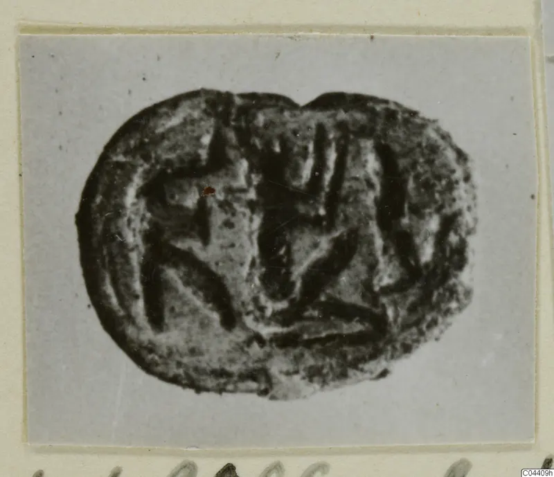 Glyptic: a dark oval seal with an incised linear design, shown in a photograph on a grey card mount