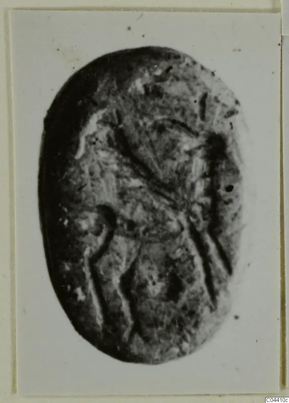Oval seal or gem of dark stone with an engraved design, shown in a photograph mounted on a card