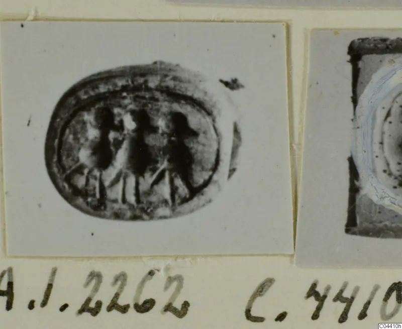 Oval seal with three upright figures engraved on its face, photographed on a card beside a second object