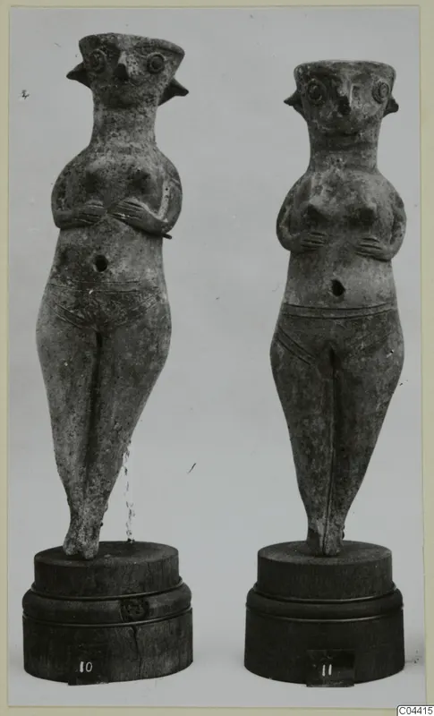 Two standing female figurines from Enkomi with hands on their chests, shown on wooden bases