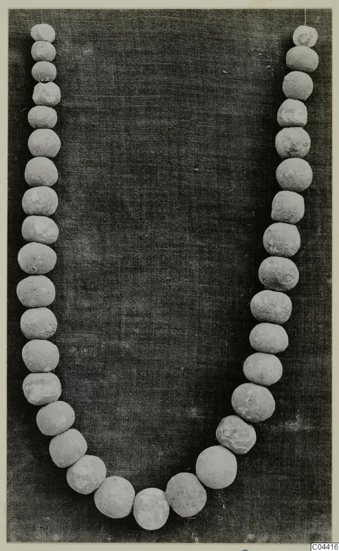 Necklace of pale, round beads laid in a U-shape on a dark cloth.