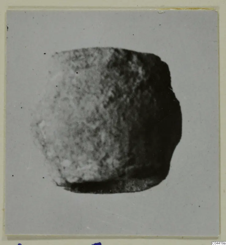 Blurred photograph of a small, rounded lead object on a grey card