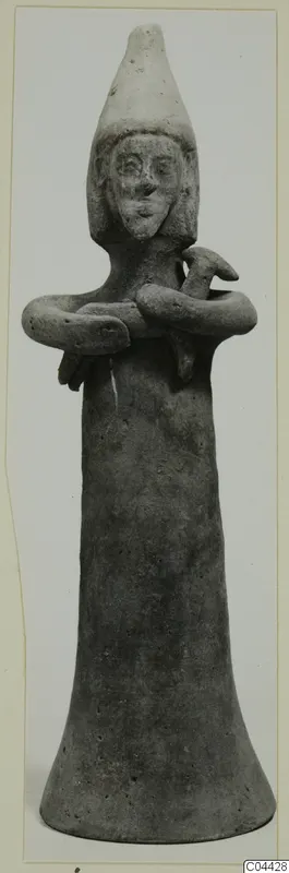 Terracotta figurine of a standing figure with a tall conical headdress and arms folded across the chest.