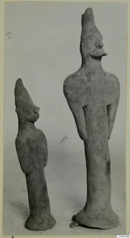 Two terracotta figurines of standing figures with tall pointed headdresses, photographed side by side against a plain grey background.