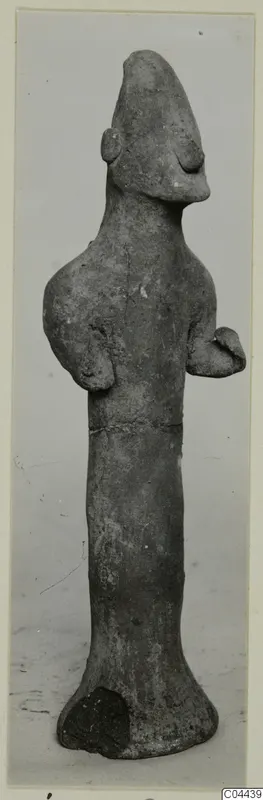 Terracotta figurine of a standing figure with a tall pointed head and arms bent at the sides