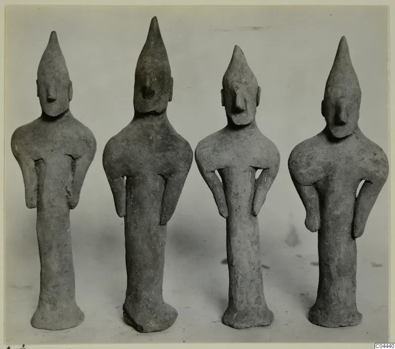 Four terracotta figurines from Ayia Irini standing in a row, each with a tall pointed head and a flared base