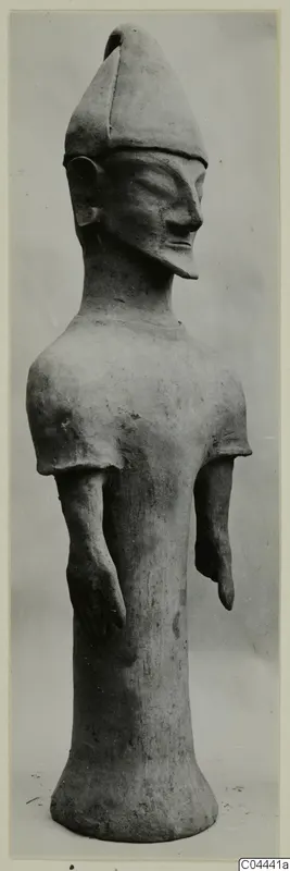 Terracotta standing figure with a tall pointed headdress and bent arms, photographed against a grey background