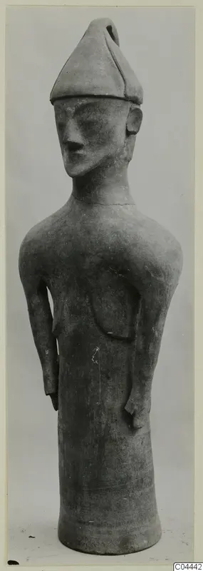 Terracotta figure from Ayia Irini with a pointed cap, long face and arms held at the sides, shown against a plain backdrop