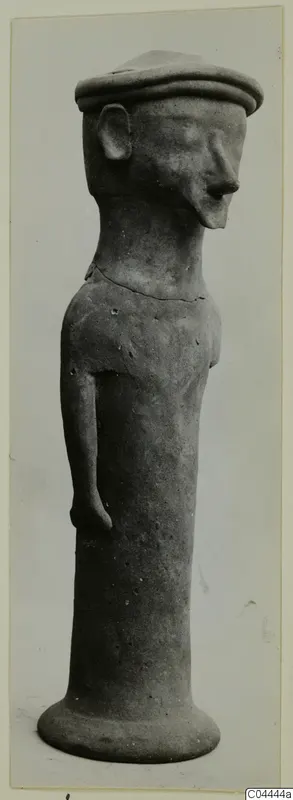 Terracotta figurine of a standing figure with a flat cap, one arm at its side and a flared base