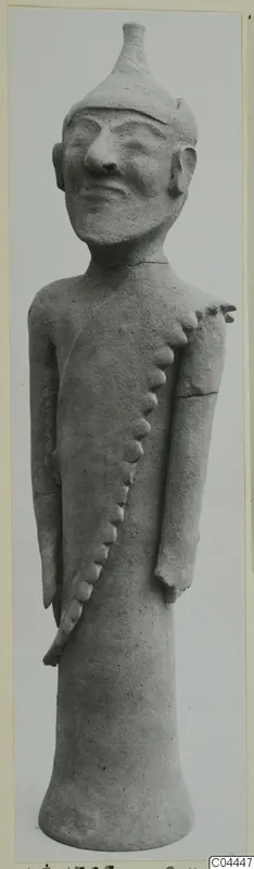 Standing terracotta figure of a man with a conical cap and a row of applied knobs running across the torso