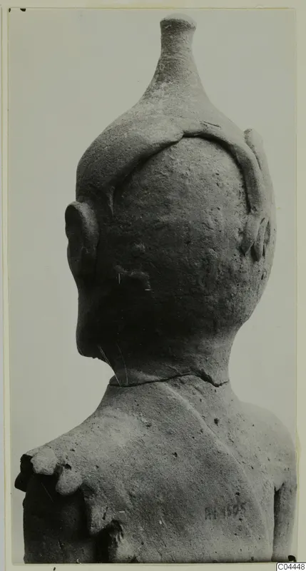 Back view of a terracotta figurine's head and shoulders, with a tall tapering headdress and rounded ears.