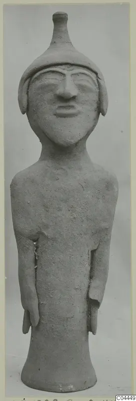 Terracotta figurine of a standing figure with a tall conical headdress, arms at the sides and a flared base