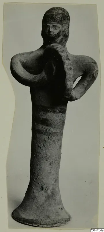 Terracotta figurine of a standing figure holding a round, ridged disc against its chest, with dark painted bands on the body