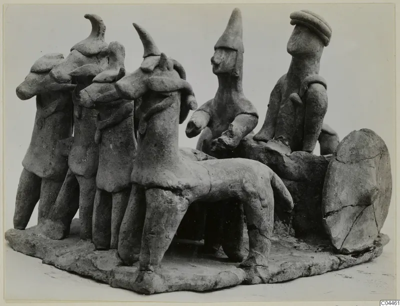 Handmade terracotta group of small figures, some with animal-like heads, beside a standing quadruped on a flat base.