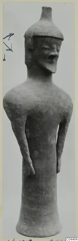 Terracotta standing figure with a flat-topped cap, bent arms at the sides and a flared base, against a grey backdrop.