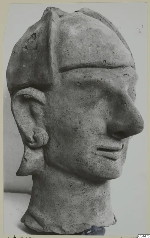 Terracotta head with a tall flat-topped cap, long nose and large ear, photographed against a grey backdrop