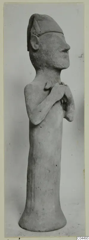 Terracotta figurine of a standing figure with a flat cap and hands clasped at the chest, shown in side view.