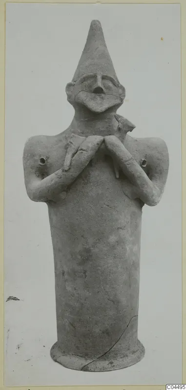 Terracotta figure with a tall cylindrical body, pointed conical head and arms folded across the chest