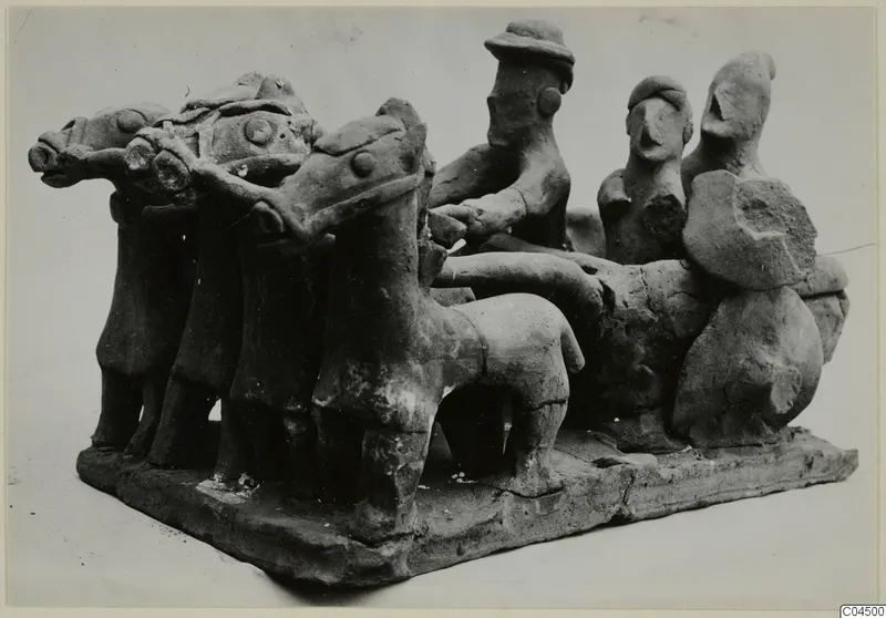 Terracotta model of a chariot drawn by three horses, with a driver holding the reins and two figures standing at the back.