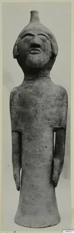 Terracotta standing figure with short stubby arms and a knob on top of its head, seen from the front.