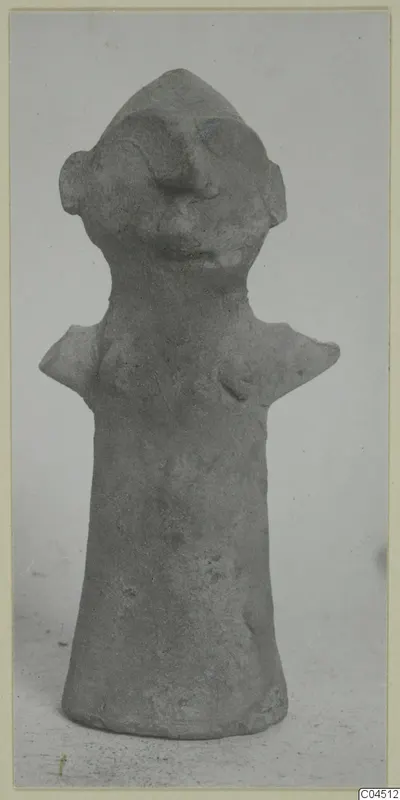 Terracotta figurine with a cylindrical body, pointed head, ear-like projections and flat shoulders, shown against a plain background
