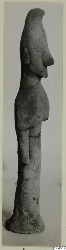 Terracotta figurine of a standing figure in profile, with a tall head, long projecting nose and a flat base