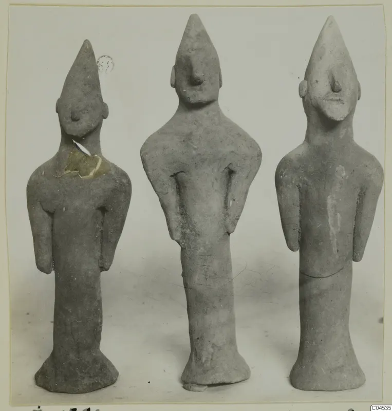 Three terracotta figurines of standing figures with pointed heads and long necks, shown side by side.