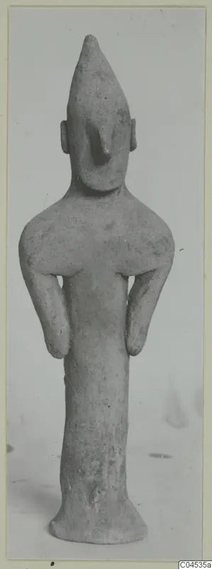 Terracotta figurine of a standing human figure with a pointed head, small ears, arms bent at the sides.