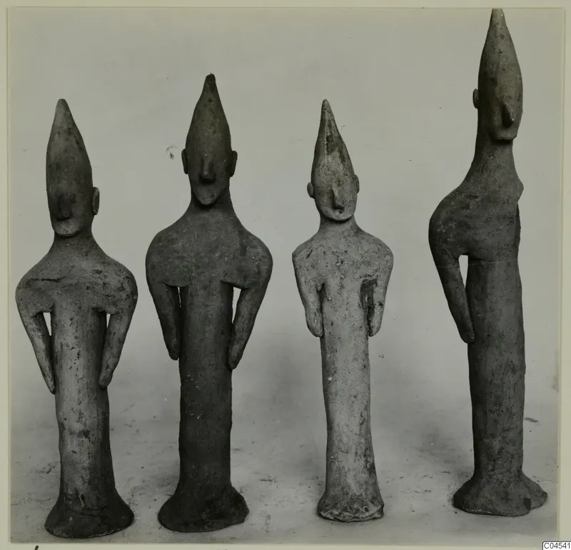 Four terracotta figurines standing in a row, with tall pointed heads and elongated bodies.